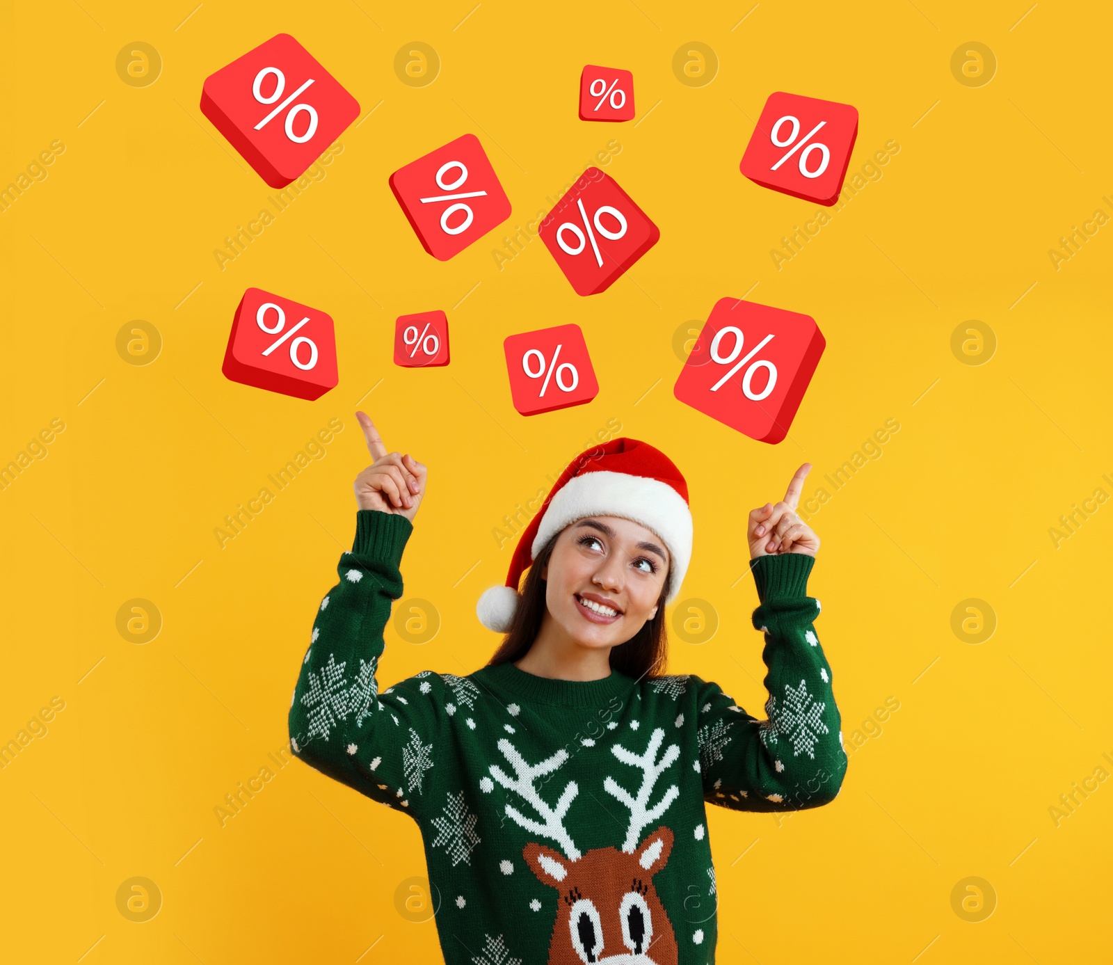 Image of Discount offer. Happy young woman in Christmas sweater and Santa hat pointing at percent signs on orange background