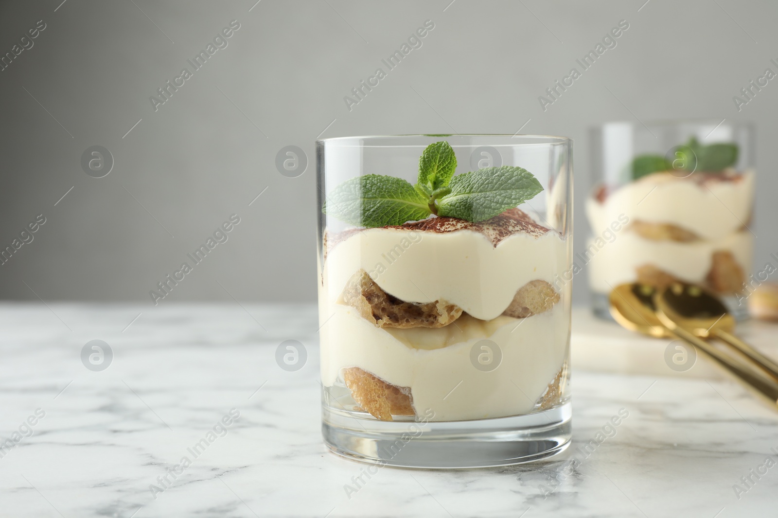 Photo of Delicious tiramisu in glasses and mint leaves on white marble table, space for text