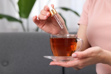 Woman dripping food supplement into cup of tea indoors, closeup. Space for text