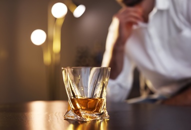 Photo of Man sitting at table with glass of whiskey, closeup. Space for text