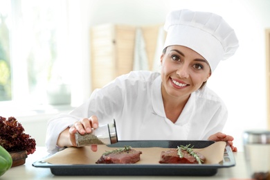 Photo of Professional female chef preparing meat on table in kitchen