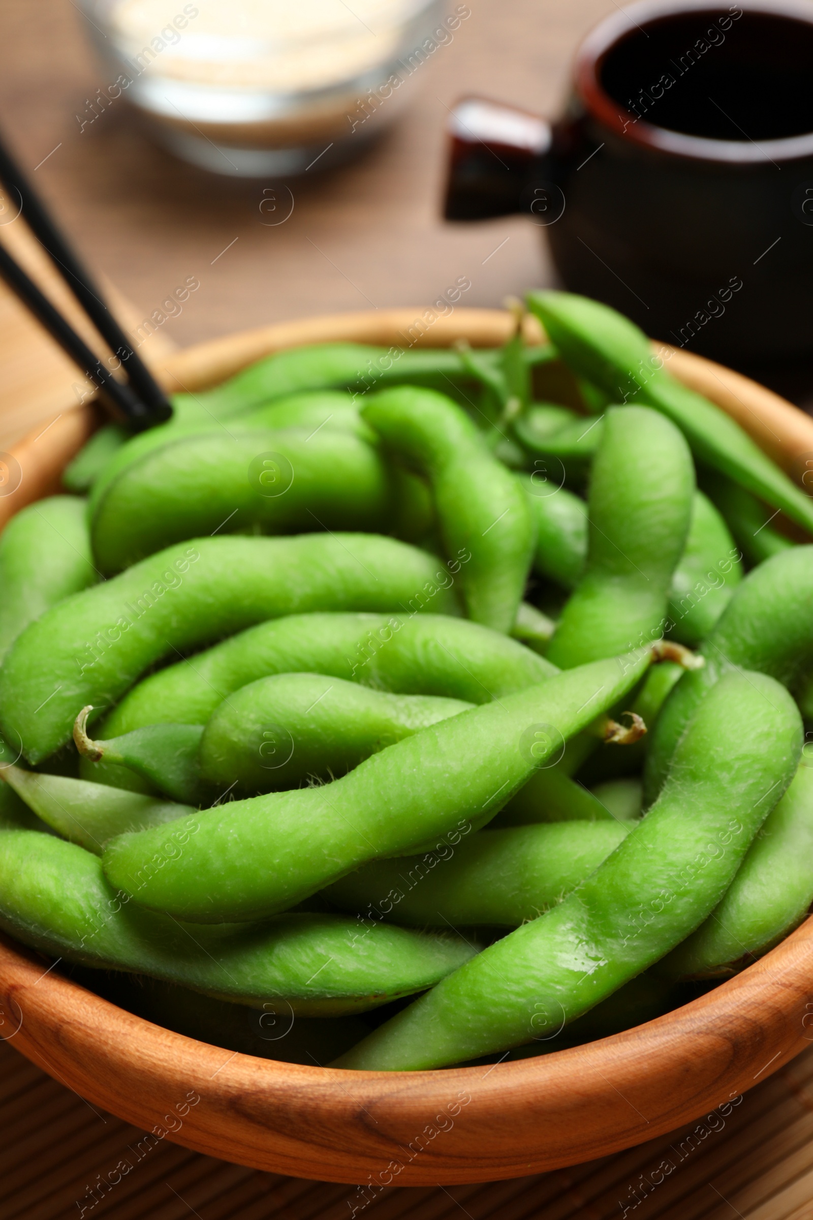 Photo of Green edamame beans in pods served on wooden table, closeup