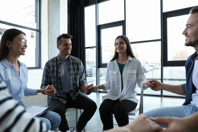 Psychotherapist holding hands with patients during group therapy session indoors