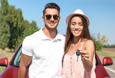 Happy young couple with key standing near new car on road