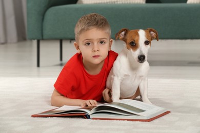 Photo of Little boy with book and his cute dog on floor at home. Adorable pet