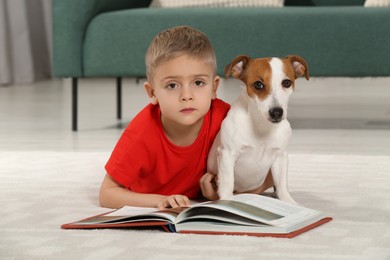 Little boy with book and his cute dog on floor at home. Adorable pet