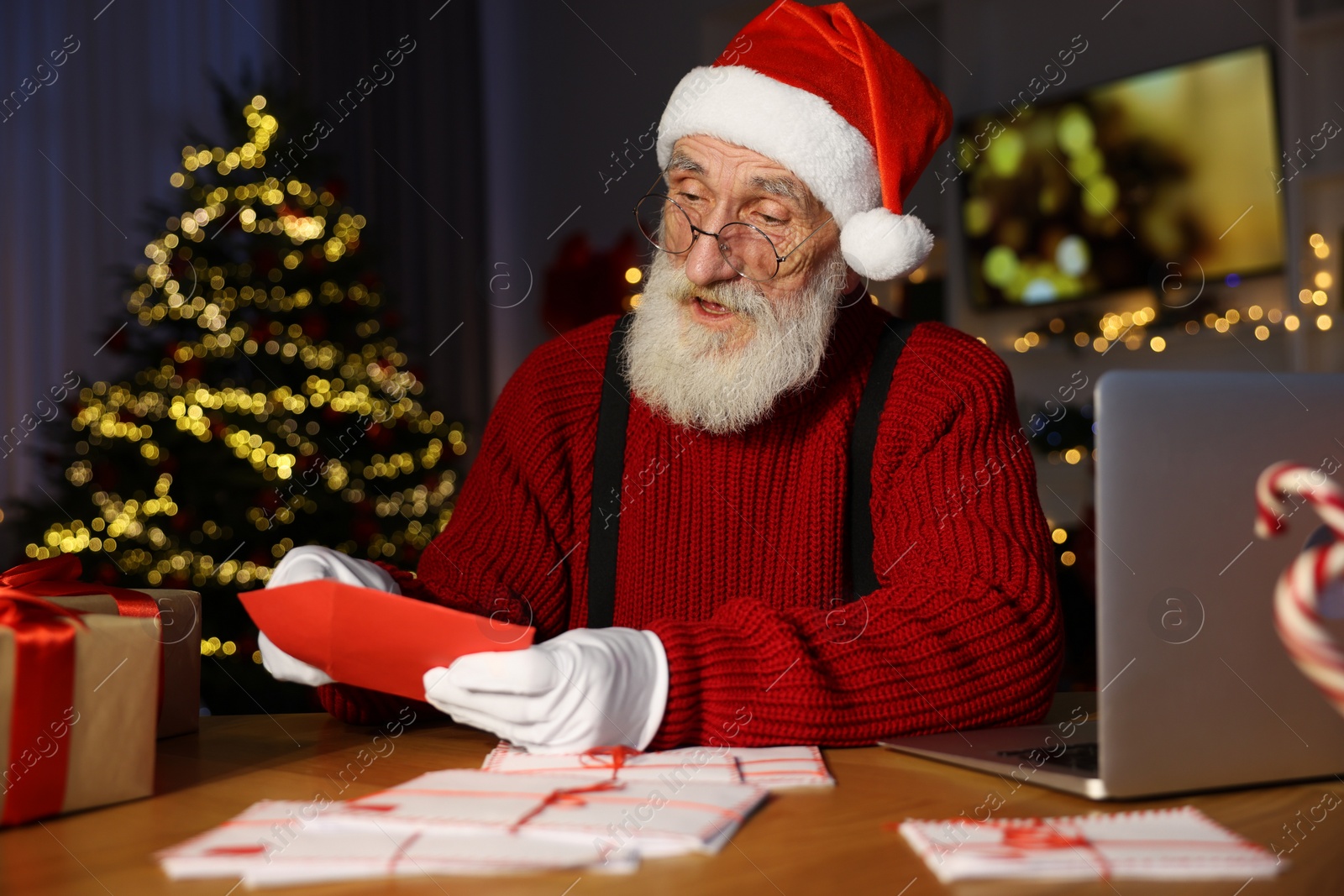 Photo of Santa Claus opening letter at his workplace in room decorated for Christmas