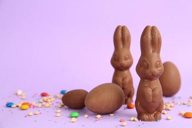 Photo of Chocolate Easter bunnies, eggs and candies on lilac background. Space for text