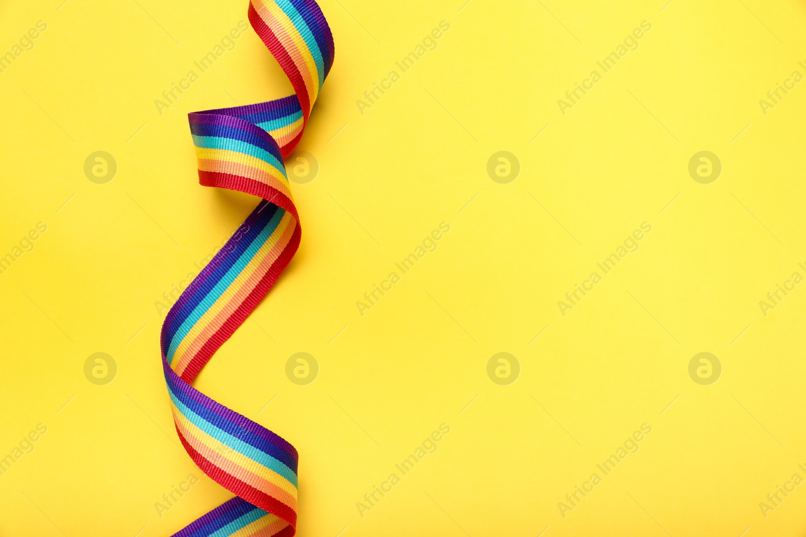 Photo of Rainbow ribbon on yellow background, top view with space for text. LGBT pride