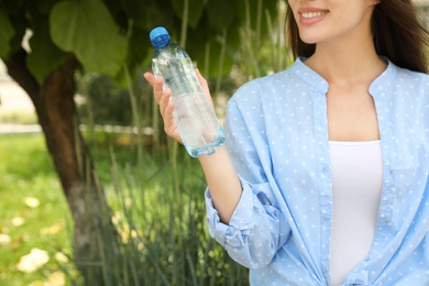 Photo of Woman with bottle of fresh water outdoors, closeup