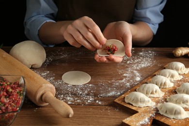 Woman making gyoza at wooden table, closeup