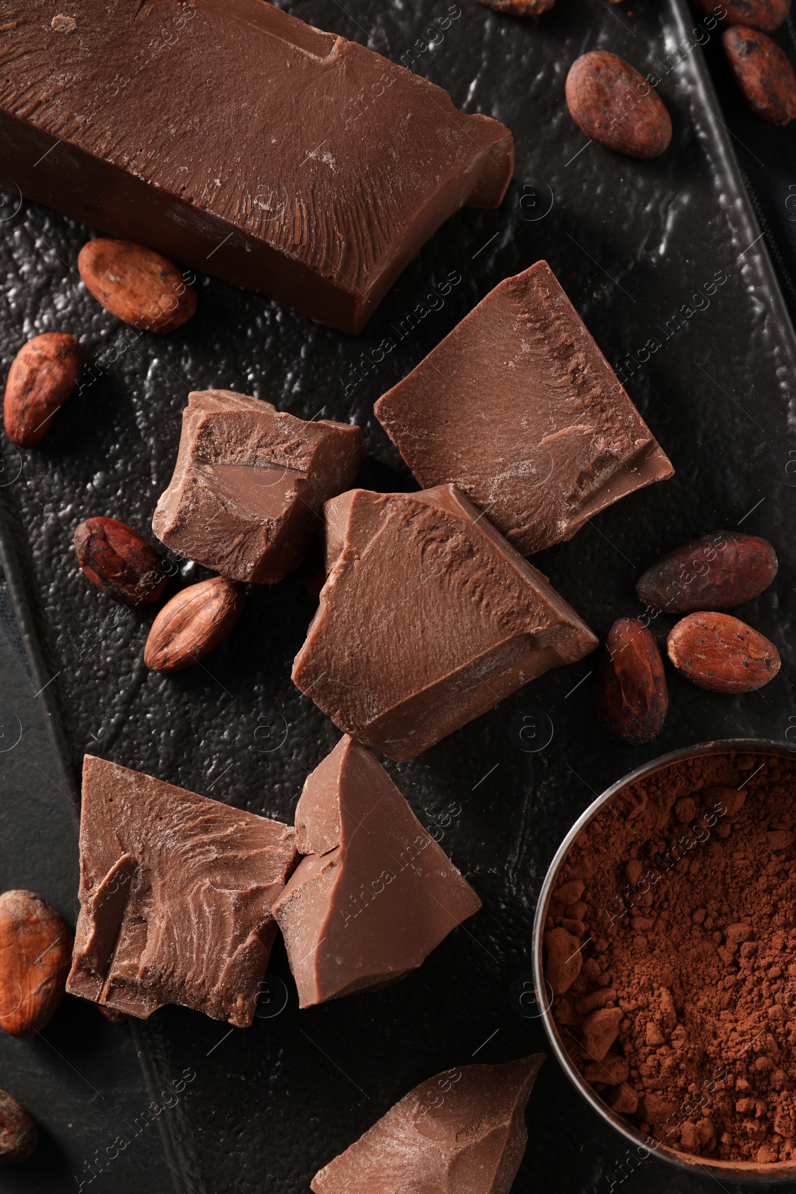 Photo of Pieces of tasty milk chocolate, cocoa beans and powder on table, top view