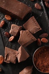 Photo of Pieces of tasty milk chocolate, cocoa beans and powder on table, top view