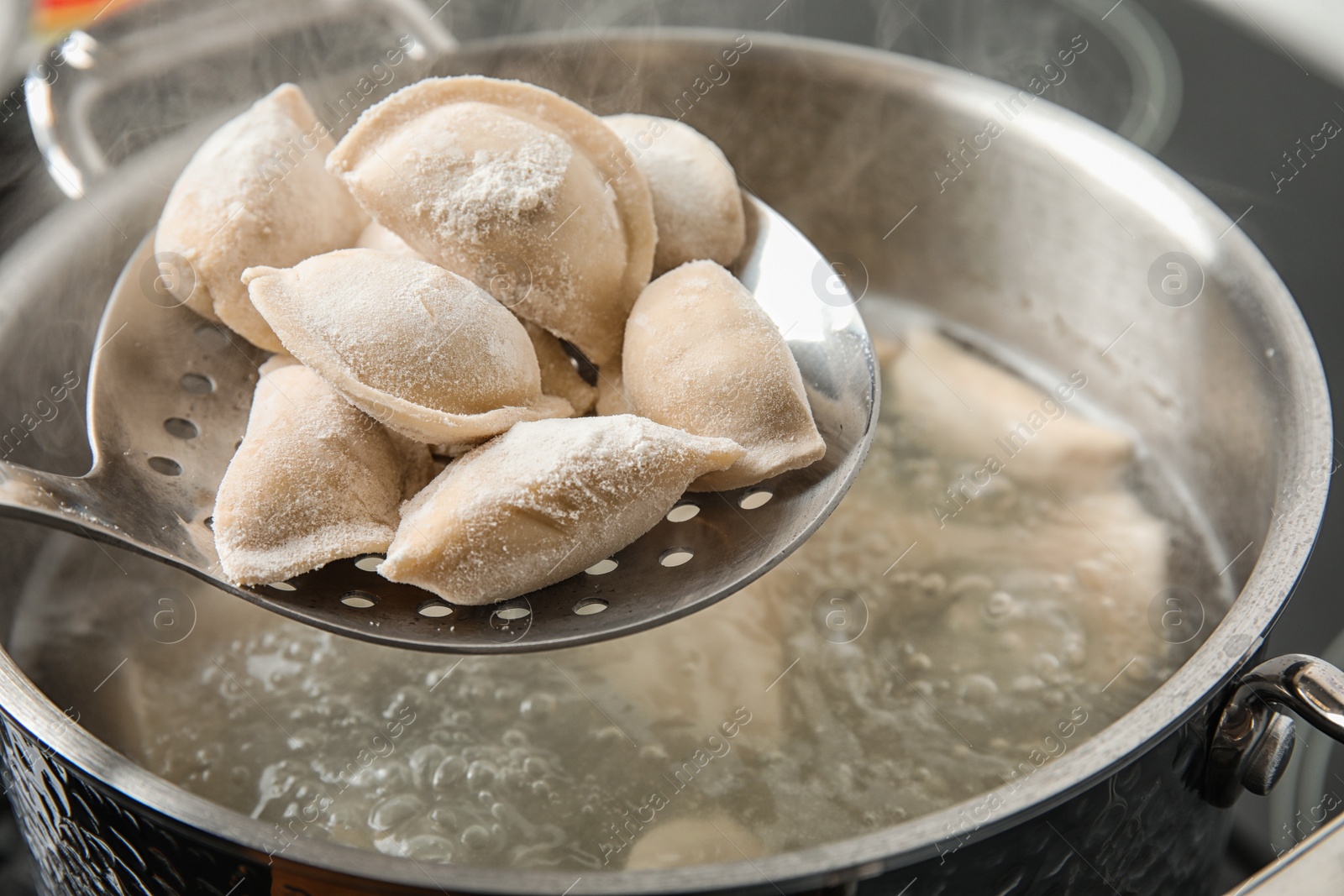 Photo of Closeup of dumplings on skimmer over stewpan with boiling water. Home cooking