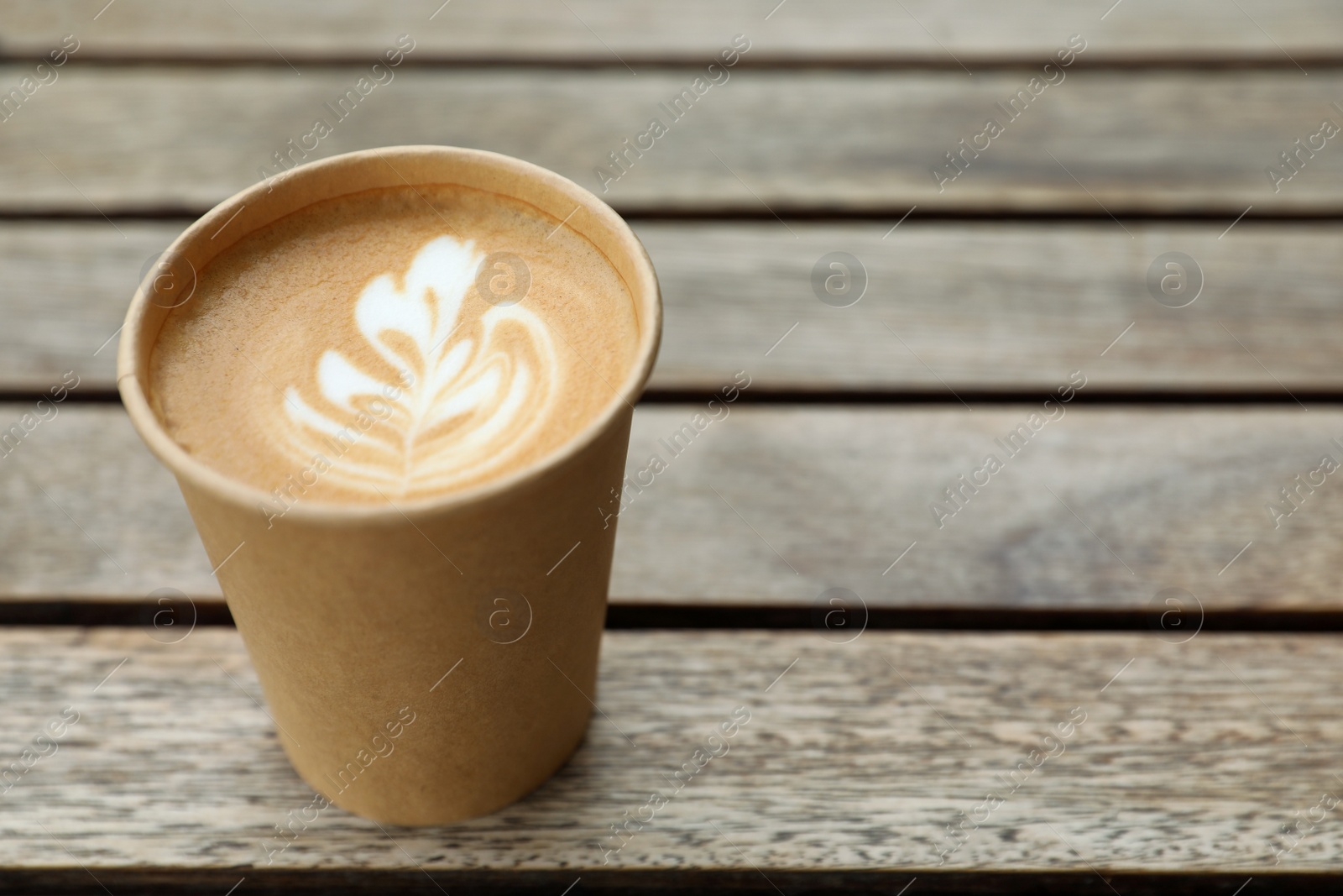 Photo of Takeaway paper cup with coffee on wooden table. Space for text