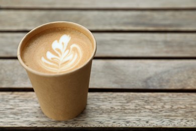 Photo of Takeaway paper cup with coffee on wooden table. Space for text