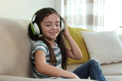 Photo of Cute little girl with headphones listening to audiobook at home