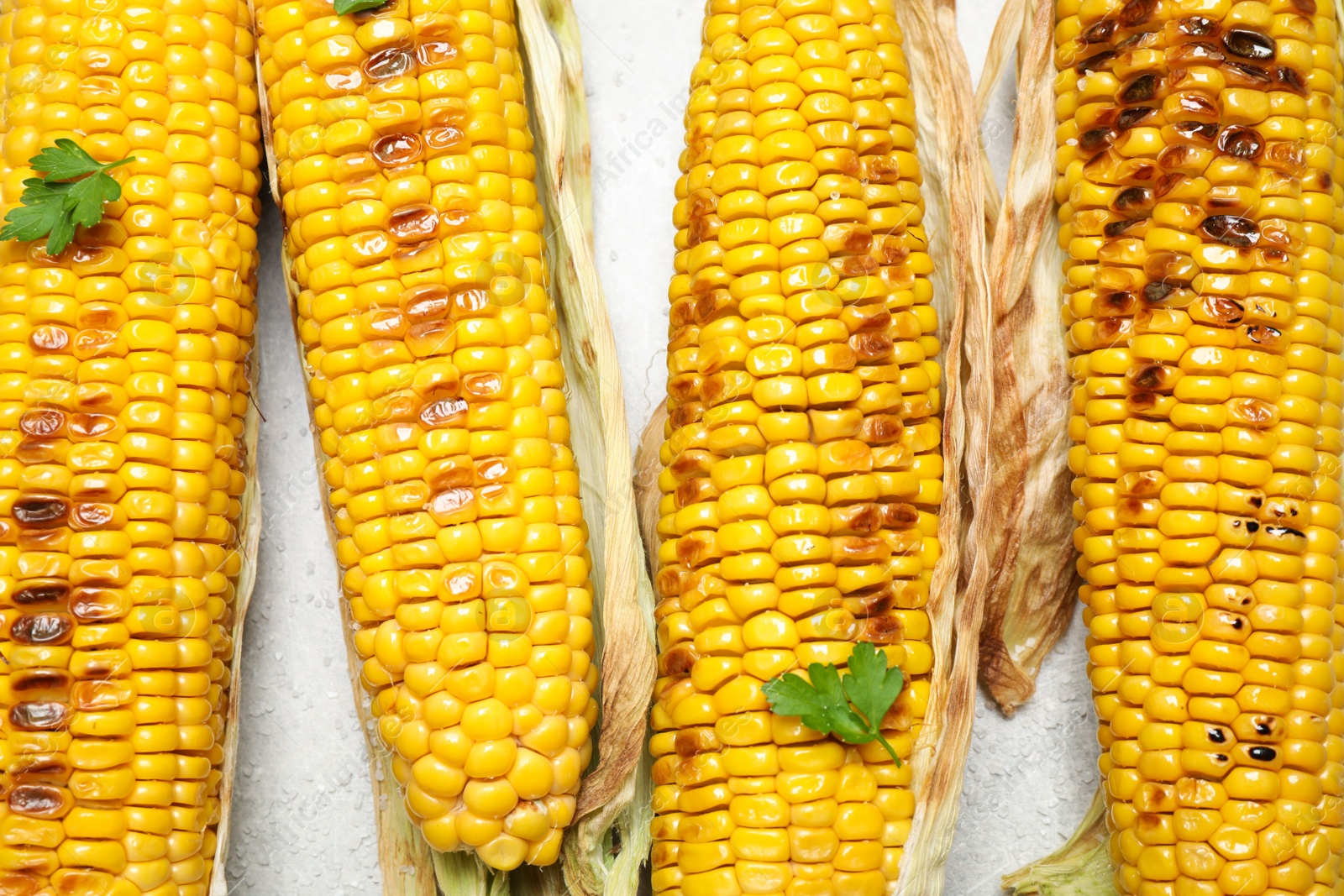 Photo of Delicious grilled corn cobs on light table, flat lay