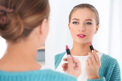 Beautiful young woman applying lipstick in front of mirror