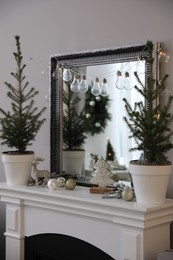 Photo of Little fir trees and Christmas decorations on mantelpiece in room. Stylish interior design