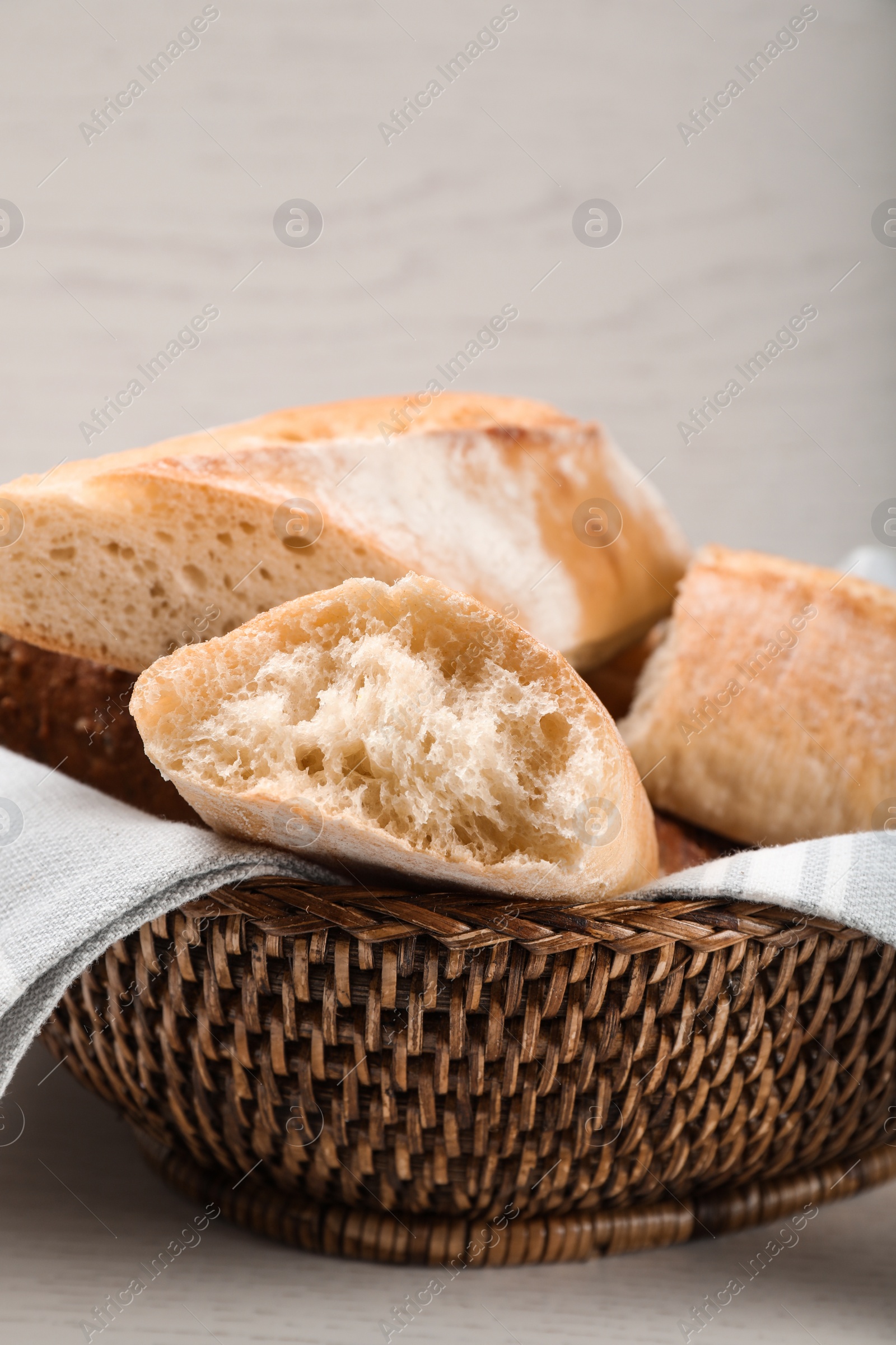 Photo of Different tasty baguettes in basket on white wooden table, closeup