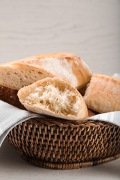 Photo of Different tasty baguettes in basket on white wooden table, closeup