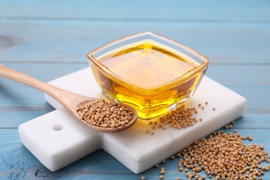 Photo of Bowl of natural oil and mustard seeds on light blue wooden table