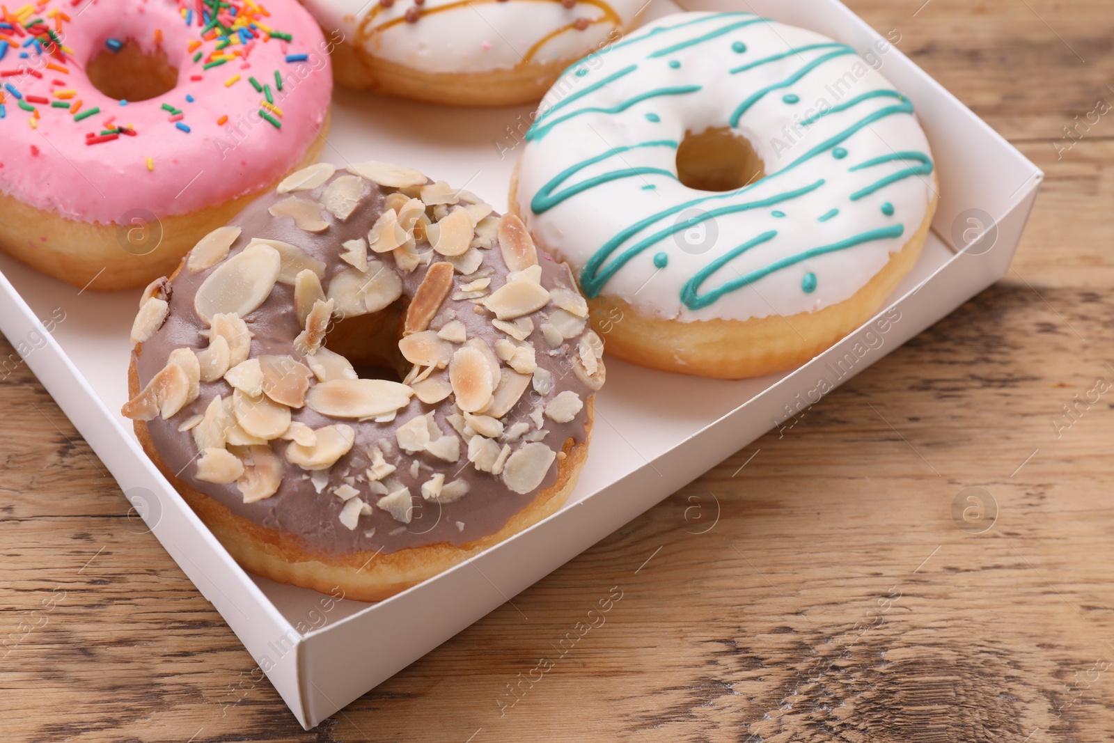 Photo of Box with different tasty glazed donuts on wooden table, closeup