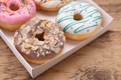 Box with different tasty glazed donuts on wooden table, closeup