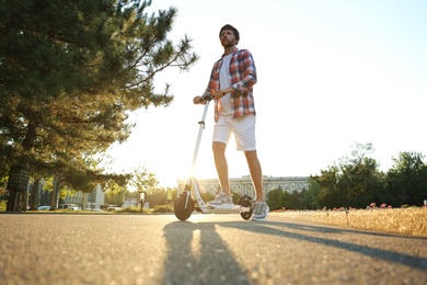 Photo of Man riding kick scooter along sunny park