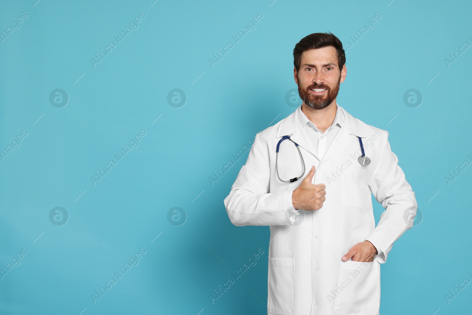 Photo of Happy doctor with stethoscope showing thumb up on light blue background. Space for text