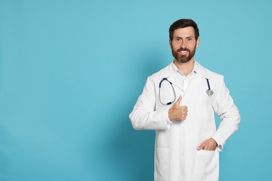 Happy doctor with stethoscope showing thumb up on light blue background. Space for text