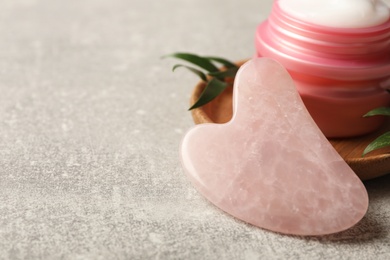 Rose quartz gua sha tool and jar of cream on grey table, closeup. Space for text