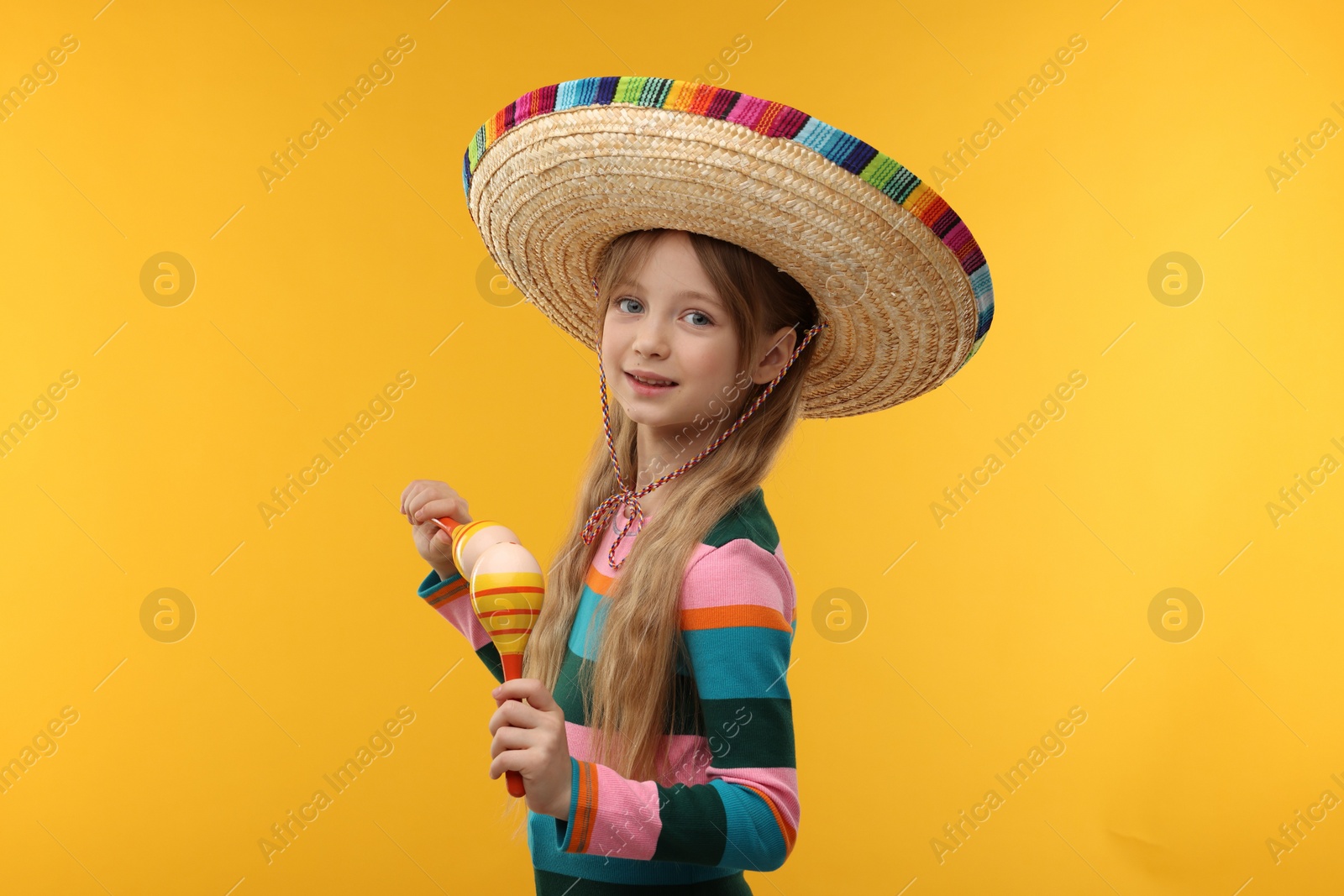 Photo of Cute girl in Mexican sombrero hat dancing with maracas on orange background