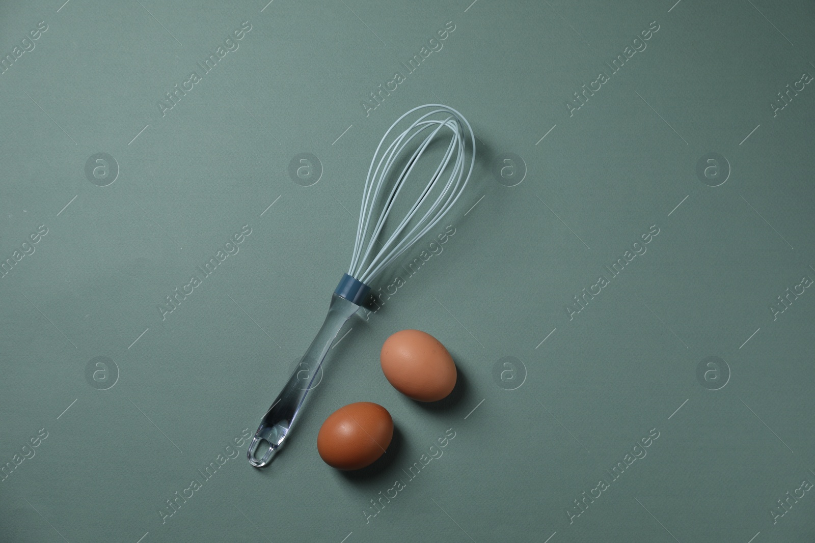 Photo of Whisk and raw eggs on pale blue background, flat lay