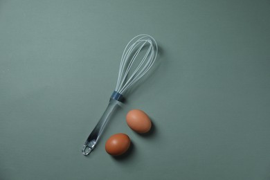 Whisk and raw eggs on pale blue background, flat lay