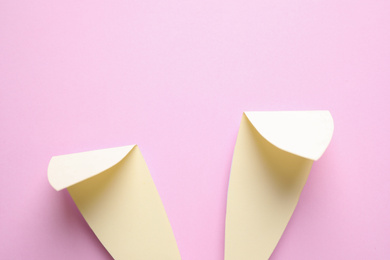 Photo of Top view of paper bunny ears on pale pink background. Easter celebration