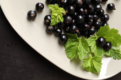 Plate with ripe blackcurrants and leaves on dark background, top view. Space for text