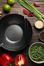 Black wok, chopsticks and products on wooden table, flat lay