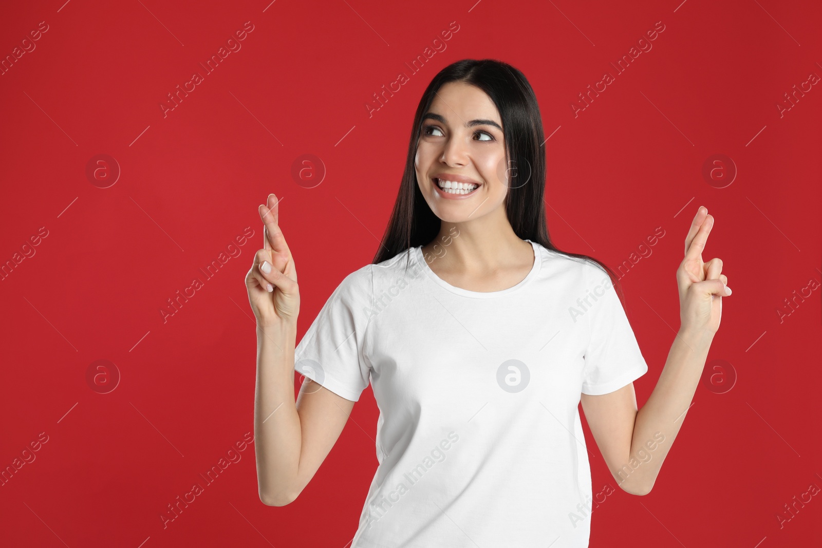 Photo of Woman with crossed fingers on red background. Superstition concept