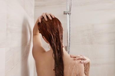 Photo of Young woman washing her hair with shampoo in shower, back view