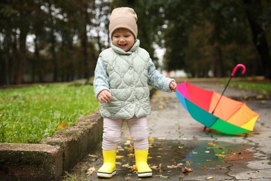Cute little girl having fun in puddle near colorful umbrella outdoors