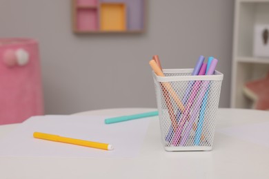 Photo of Holder with different markers and sheet of paper on white table, space for text. Stylish kindergarten interior