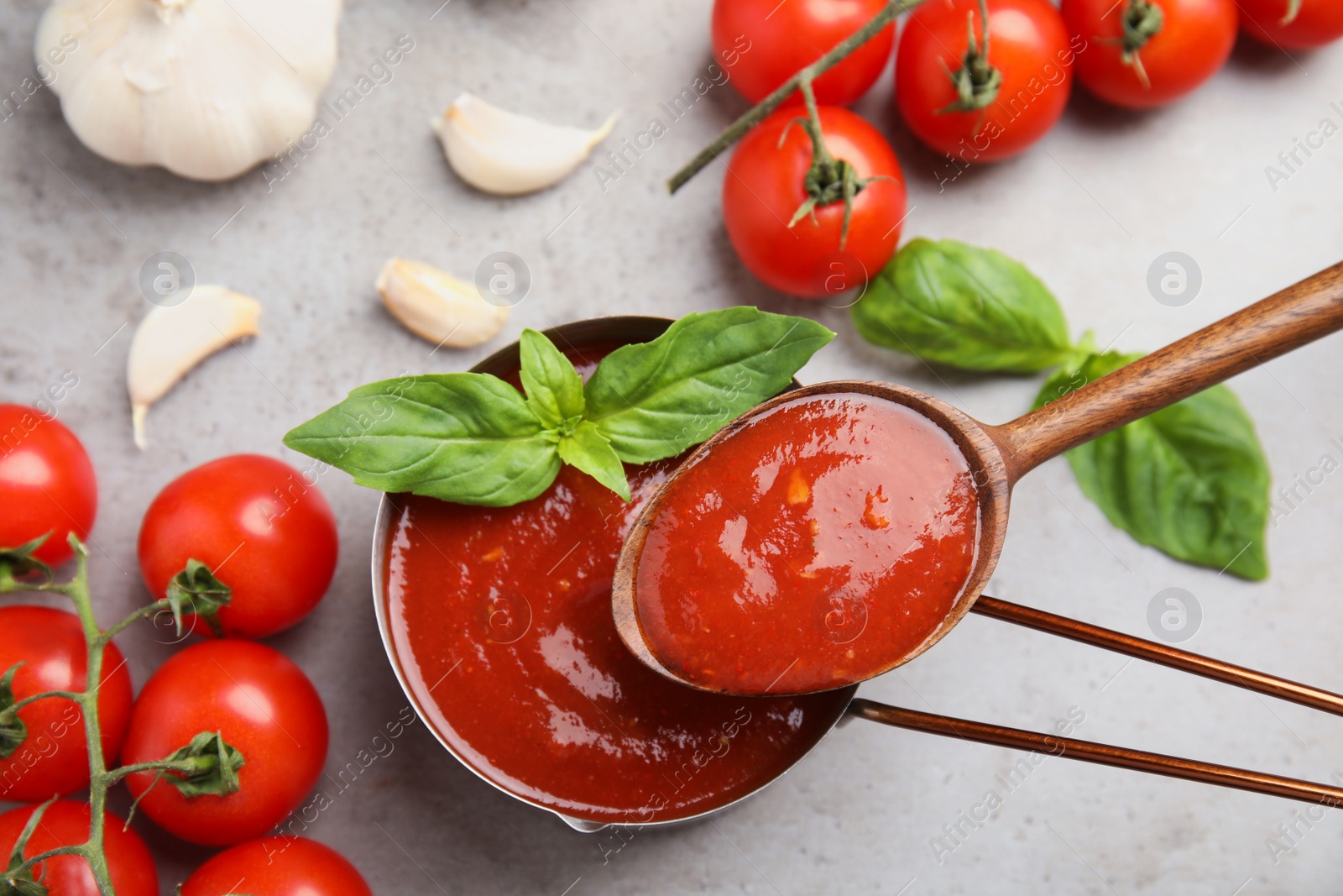 Photo of Flat lay composition with spoon and pan of tomato sauce on grey table