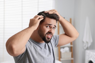 Photo of Emotional man with dandruff in his dark hair in bathroom