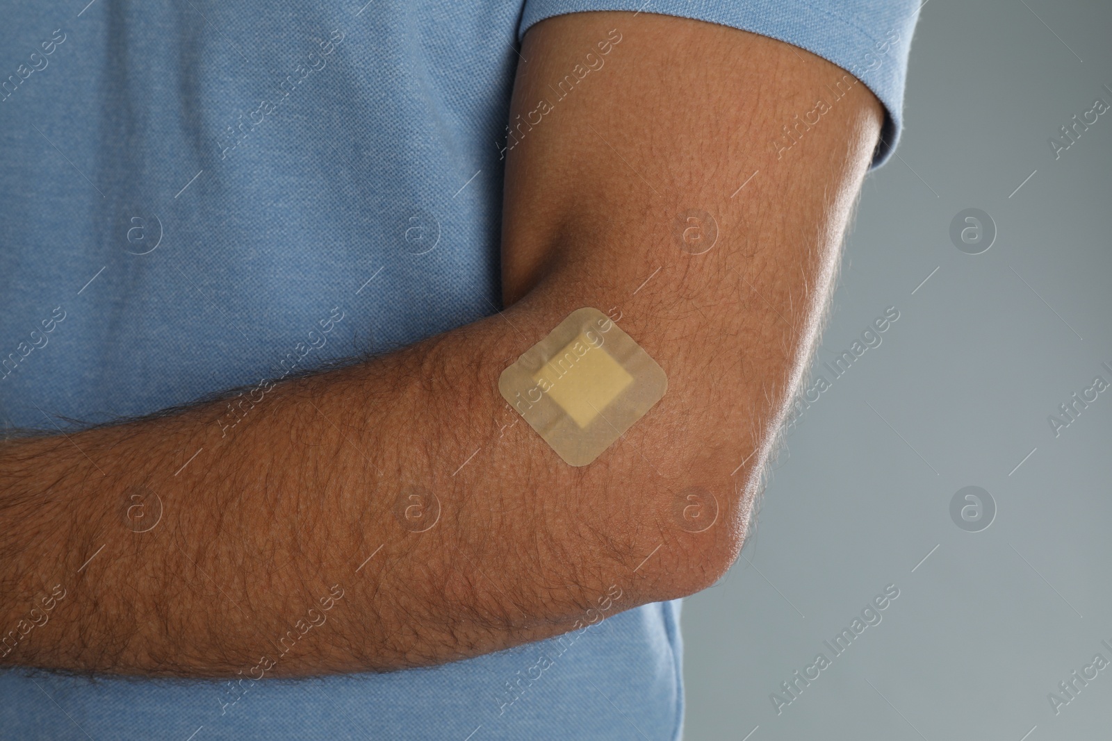 Photo of Man with sticking plaster on arm against light grey background, closeup