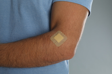 Photo of Man with sticking plaster on arm against light grey background, closeup