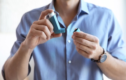 Photo of Young man with asthma inhaler indoors, closeup