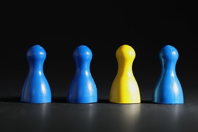 Photo of Choice concept. Yellow pawn among blue ones on black table, closeup