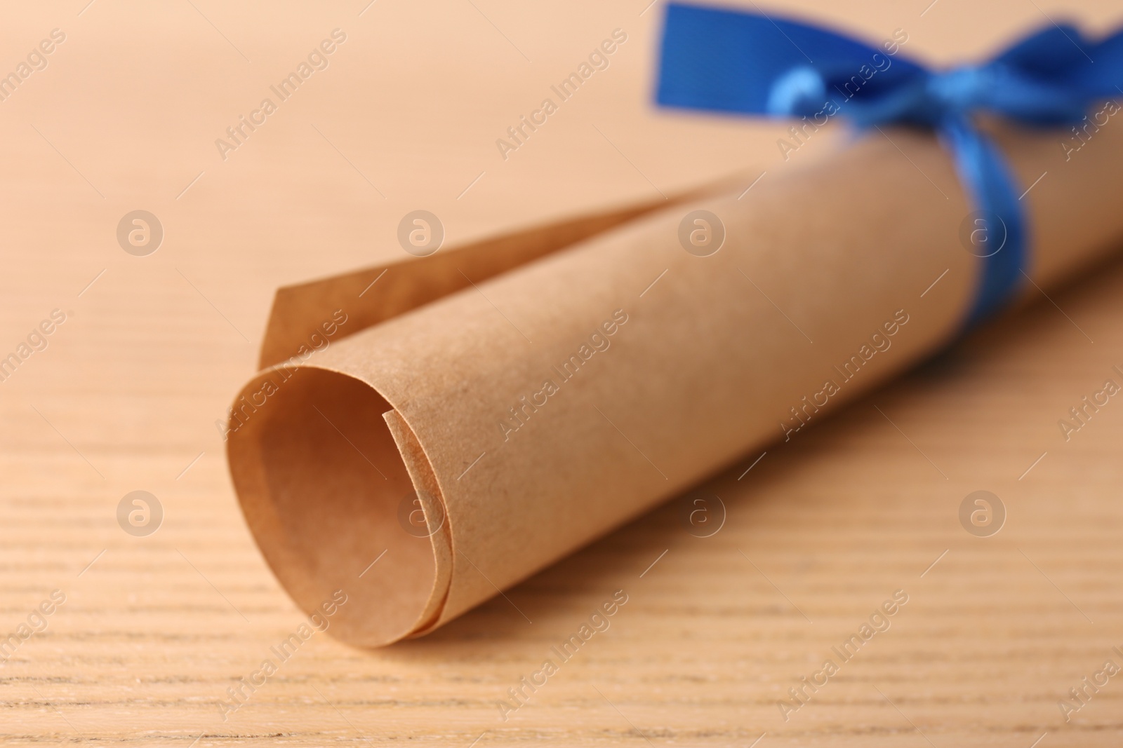 Photo of Graduation diploma tied with blue ribbon on wooden table, closeup